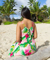Woman in a floral Hawaiian dress sitting on a beach with palm trees in the background